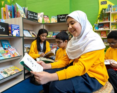 Pupils wearing yellow jumpers in a primary school library reading a diverse range of materials.