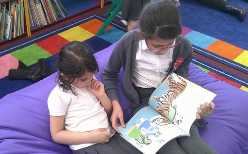 Girls sharing a book sitting on a school library beanbag