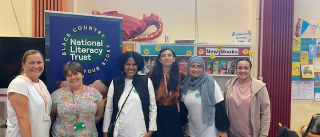 a group of woman smiling at the camera with a table in front of them and a row of books behind them.