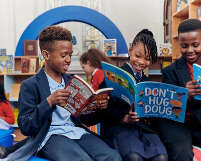 Three primary school children sit in their newly transformed library and enjoy looking at books together.