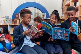 Three primary school children sit in their newly transformed library and enjoy looking at books together.