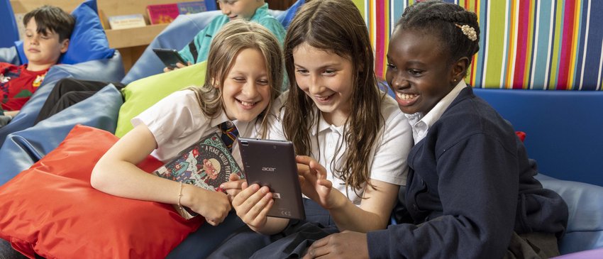 Children sit and enjoy a book and a digital screen in a comfy school library space