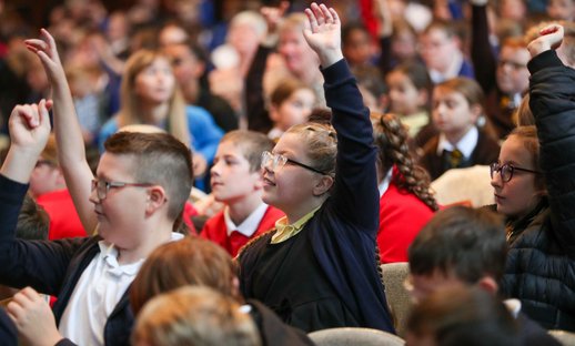 Children with their hands up in an a big assembly event
