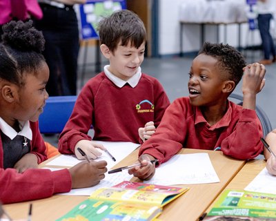 Three primary school children reading, writing and speaking to each other