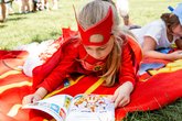 Child in fancy dress reads a book outside at a community event in Stoke-on-Trent