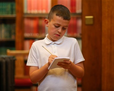 Primary school boy writing with library background