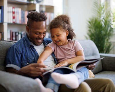 An image of a child looking and laughing at books with her dad