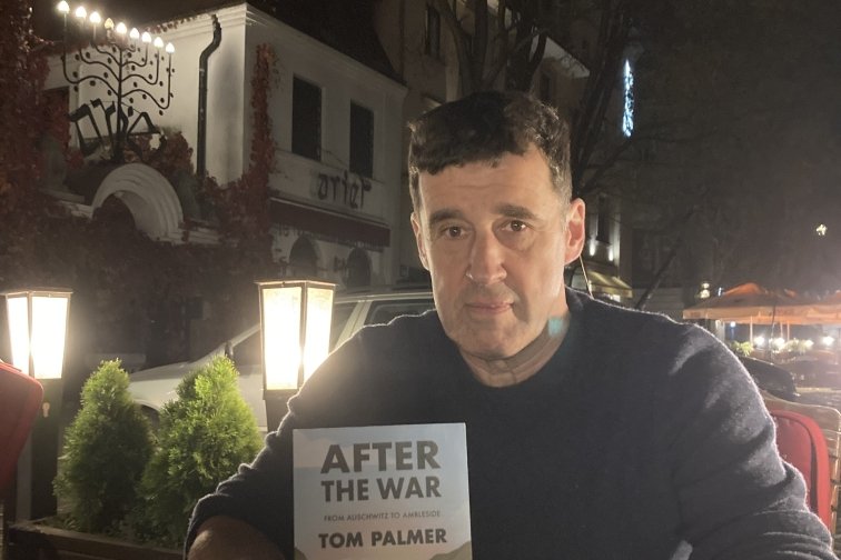 Tom Palmer author holds his book titled After the War, sitting outside in the evening