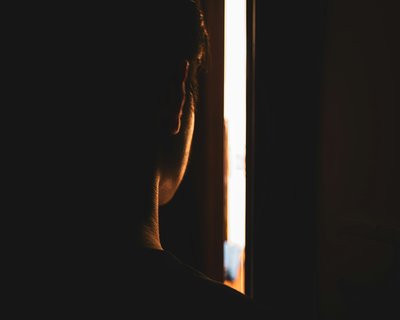 Person peers through the gap of a slightly opened door from a dark room into a light space